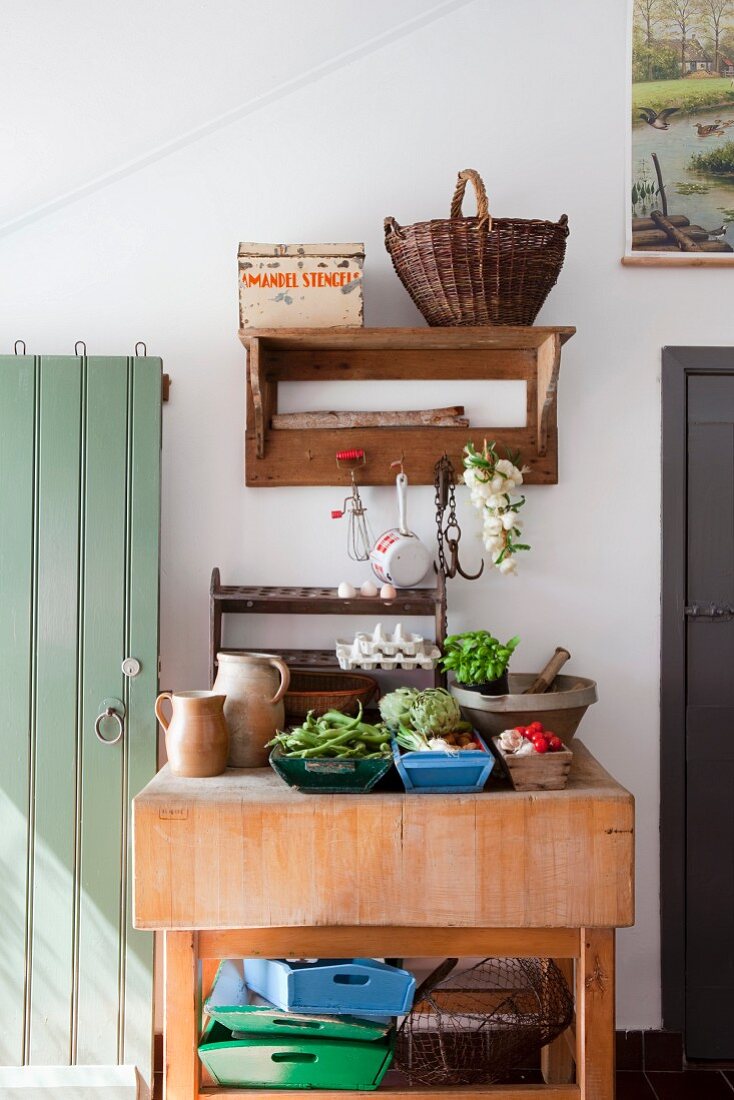 Rustikaler Küchentisch aus Holz, darauf frisches Gemüse und Küchenutensilien, an Wand aufgehängtes Holzbord