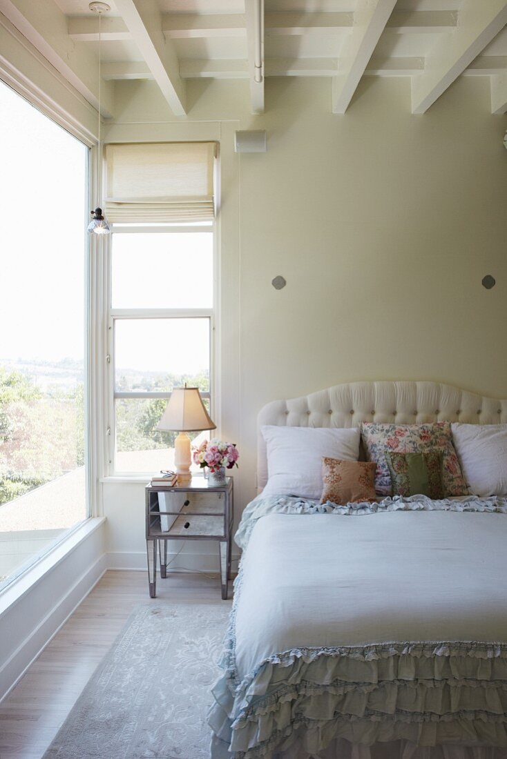Bett mit gepolstertem Kopfteil und Rüschen Tagesdecke in Schlafzimmer mit weisser Holzdecke