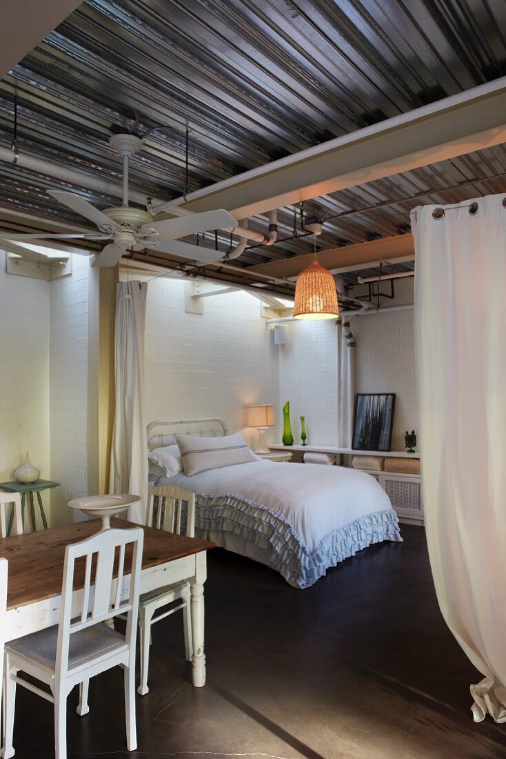 Essplatz vor offenem Schlafbereich, seitlich Vorhänge mit Blick auf Doppelbett und Rüschen Tagesdecke