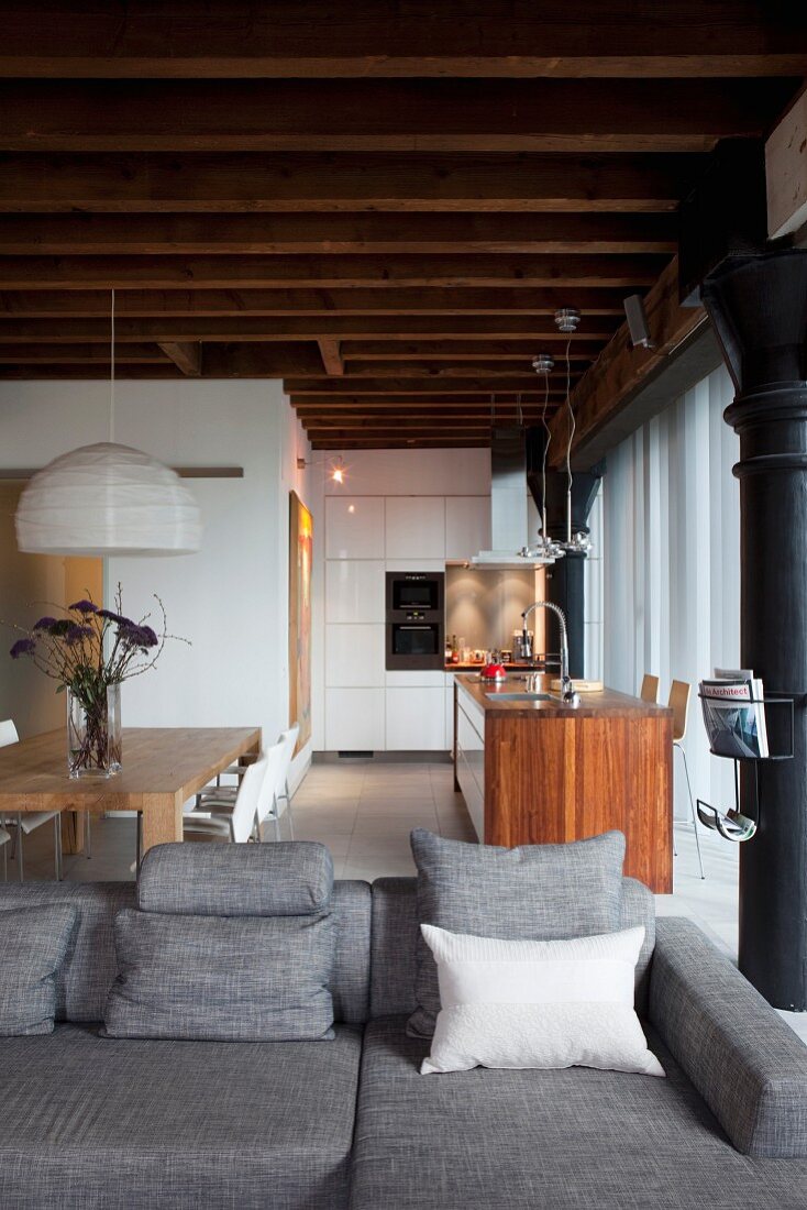Gemütliche Couch in edlem Grau, dahinter Essplatz und Kochbereich mit freistehender Theke in Loftwohnung