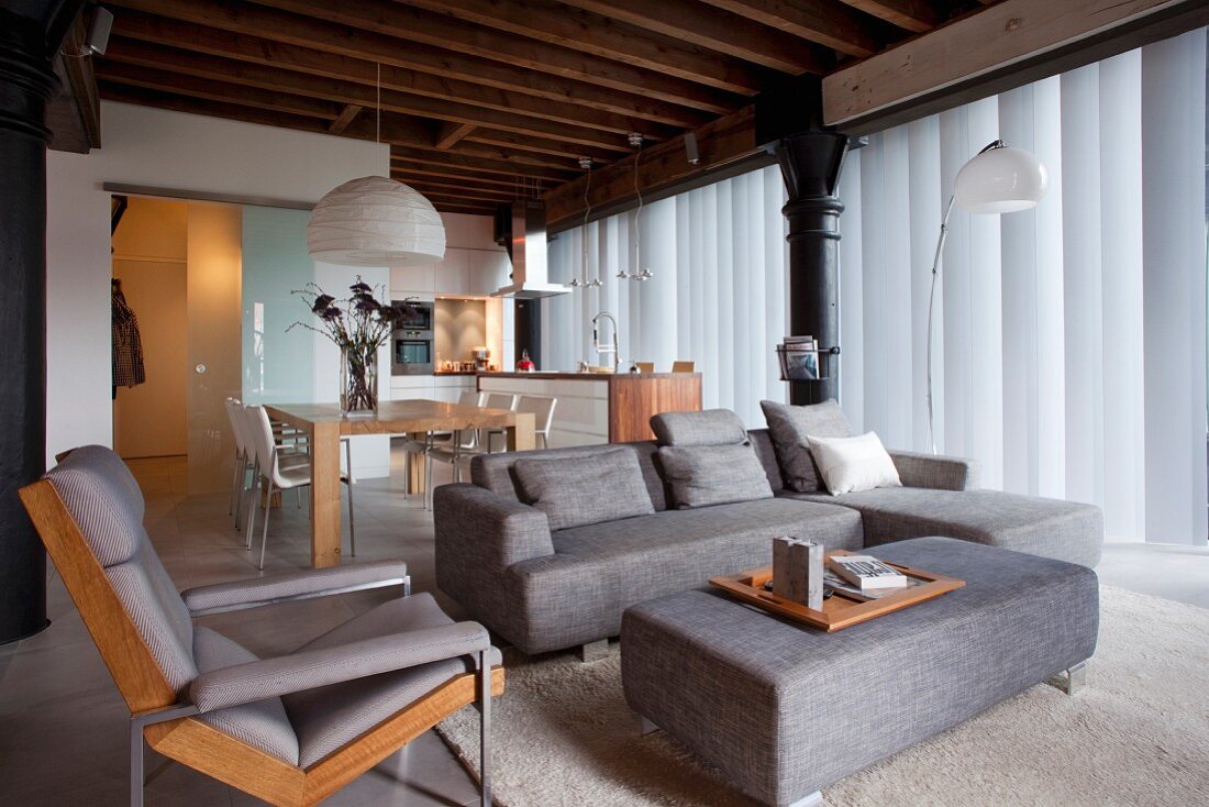 Loungebereich mit grauem Sofa und passendem Polster-Couchtisch, dahinter Essplatz in eleganter Loftwohnung