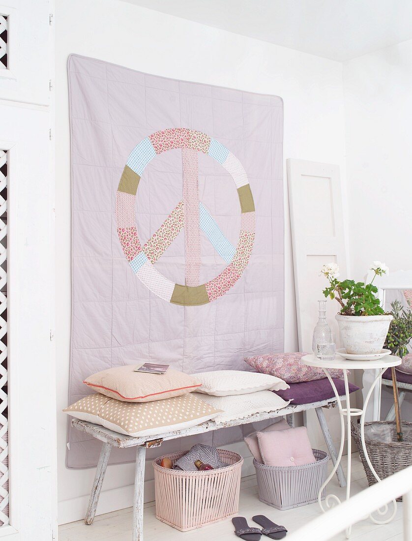 Hand-sewn, pastel wall hanging with peace motif above vintage bench with scatter cushions