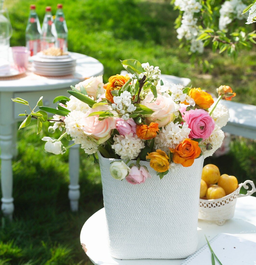 Bunter Frühlingsstrauss mit verschiedenfarbigen Ranunkeln und weißem Flieder auf Gartentisch