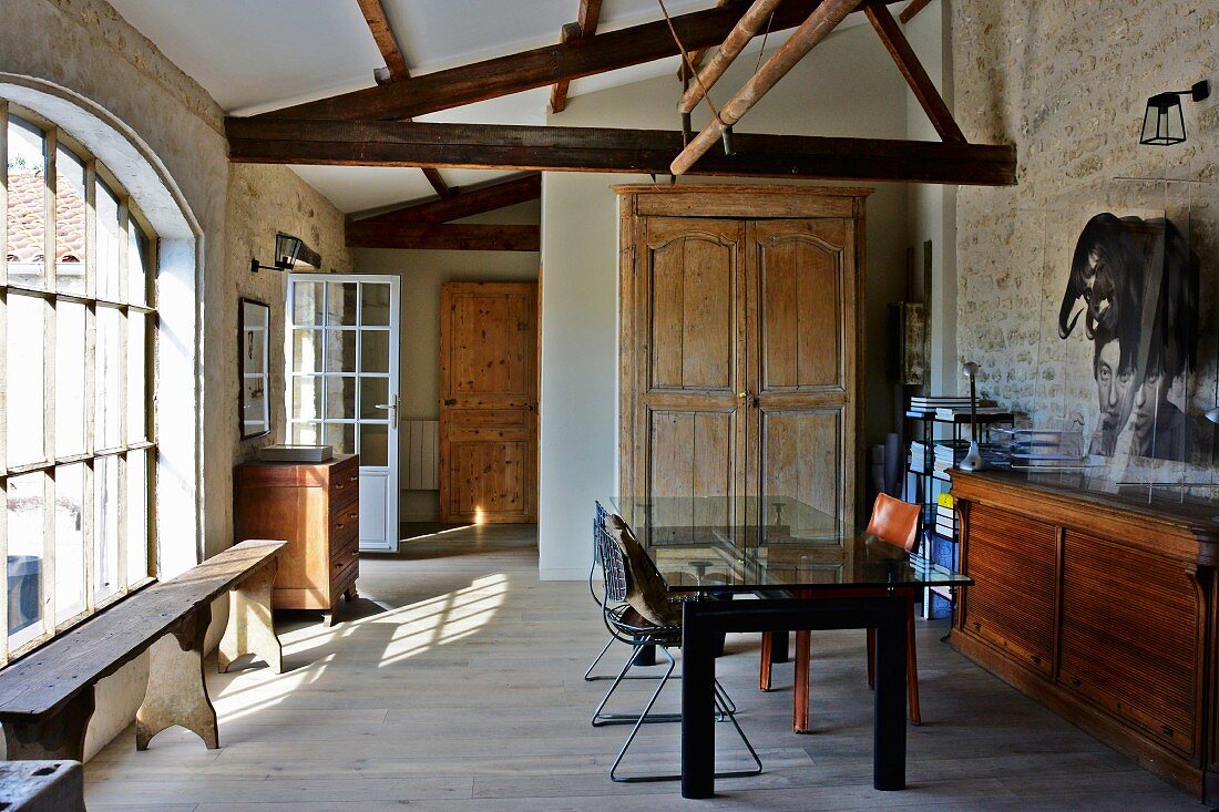 Teilrenovierte Scheune - Schlichte Möblierung im Stilmix, moderner Tisch vor Holztruhe, seitlich rustikale Holzbank vor Sprossenfenster