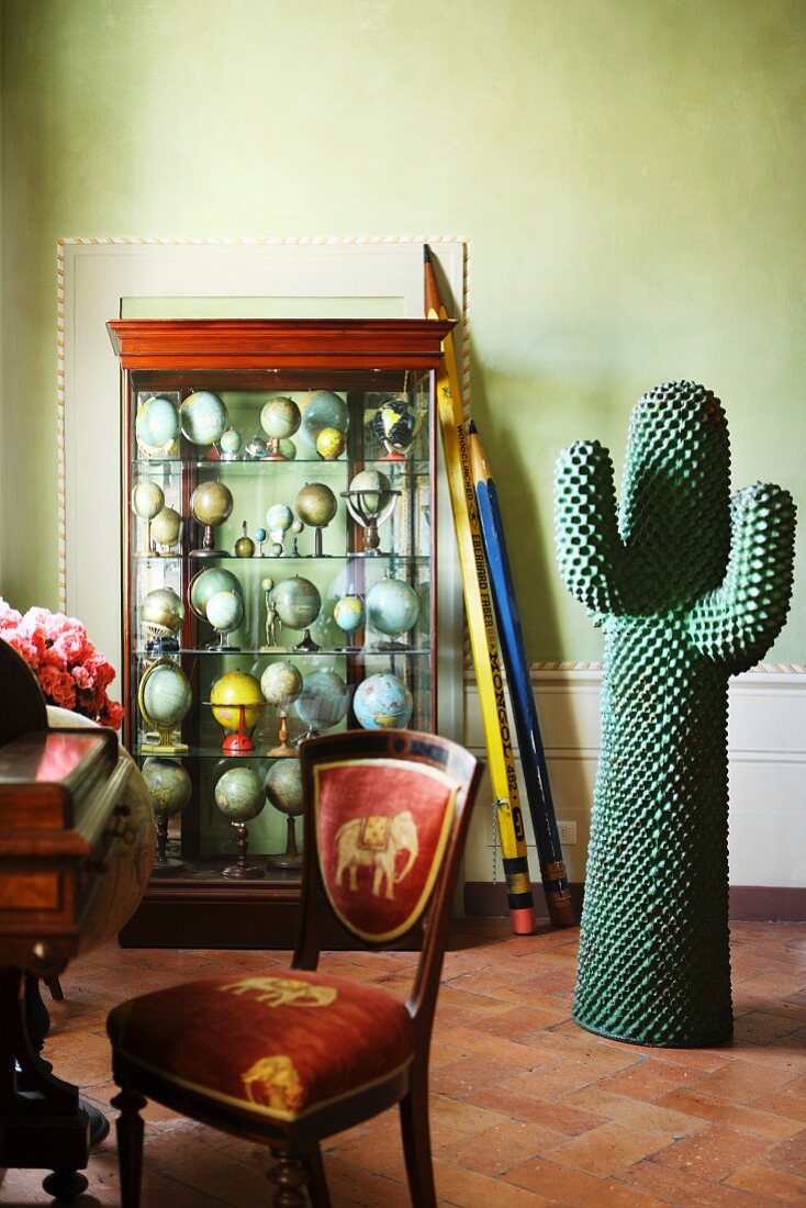 Überdimensionale Bleistifte, angelehnt an Vitrinenschrank mit Globen und Kaktusfigur in einer Altbauwohnung
