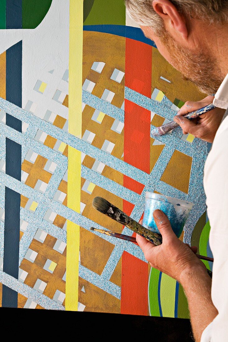 Künstler mit Pinsel und Farbtopf beim Finish einer grafisch bunten Wandgestaltung