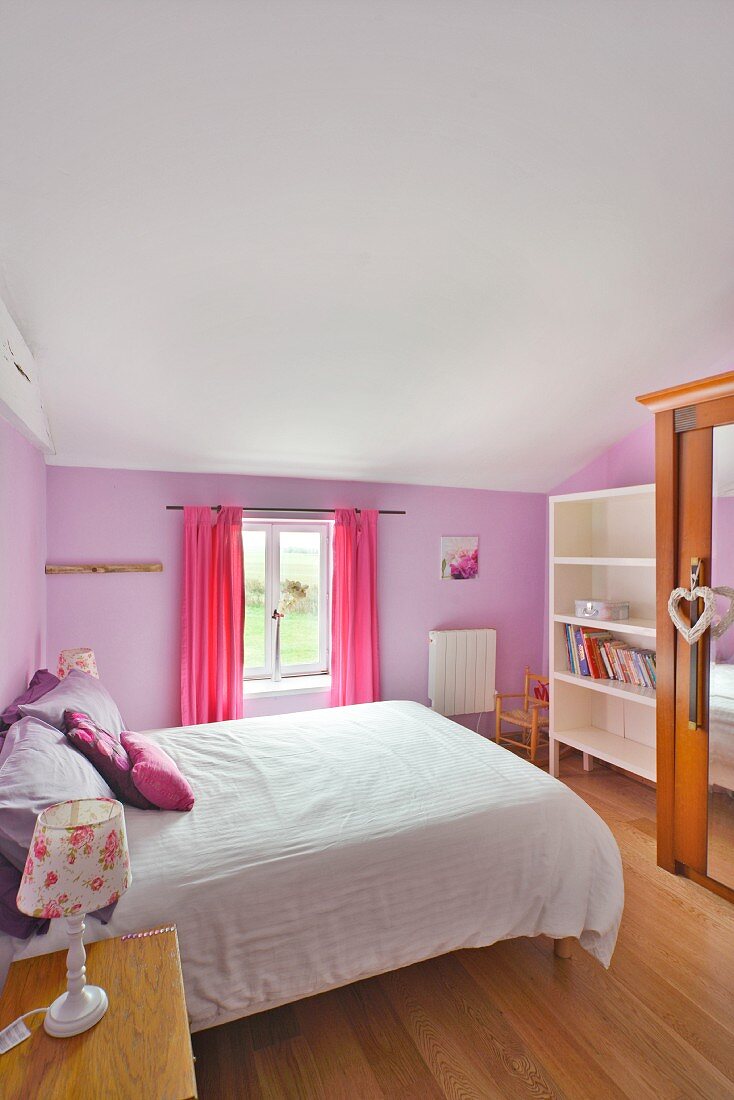 Romantisches Schlafzimmer mit pastellviolett getönter Wand und Textilien in Pink und Lila