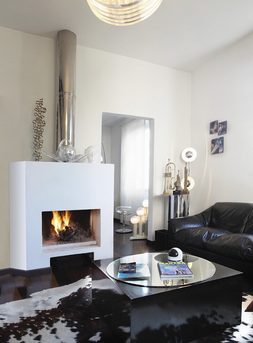 Leather couch and coffee table with round mirrored top on cowhide rug in front of open fire