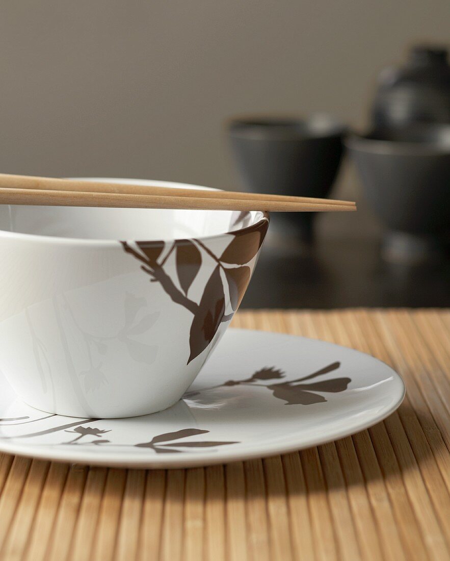 Chopsticks and china bowl with brown leaf motif on bamboo placemat