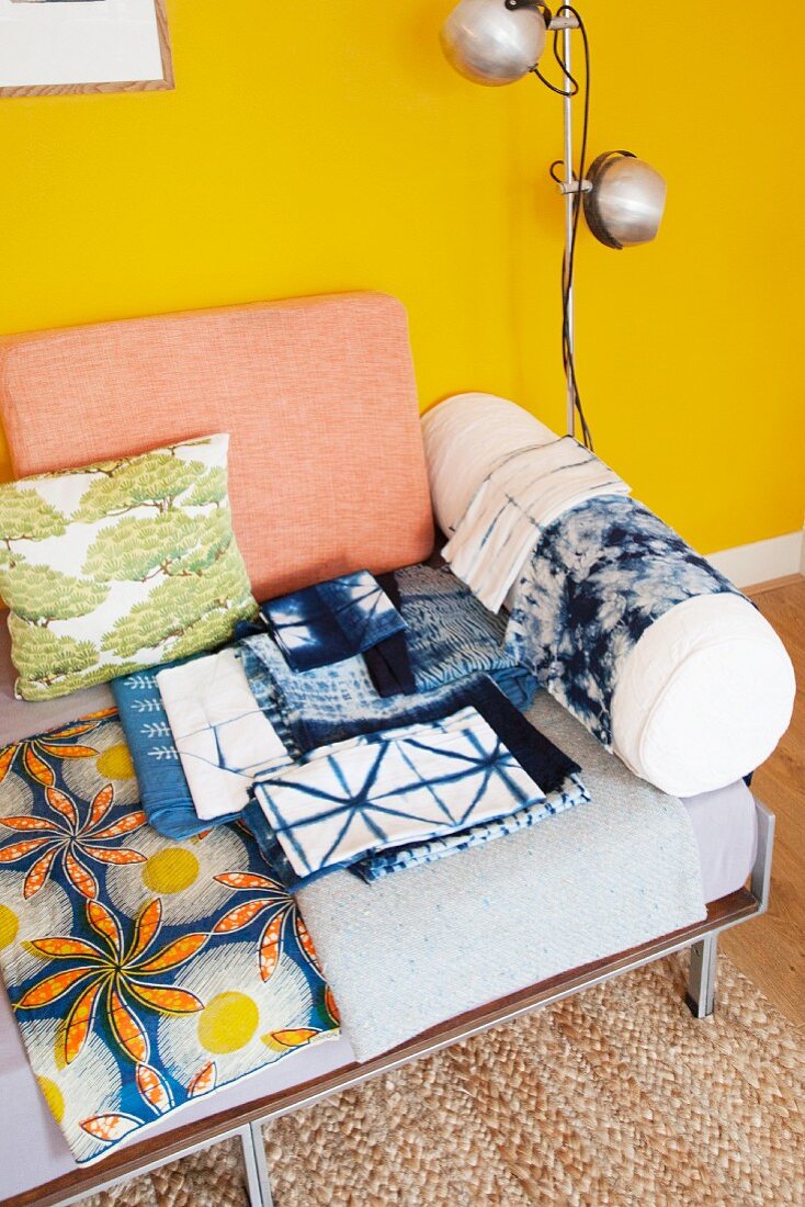 Batik fabrics on couch with cushions against yellow wall