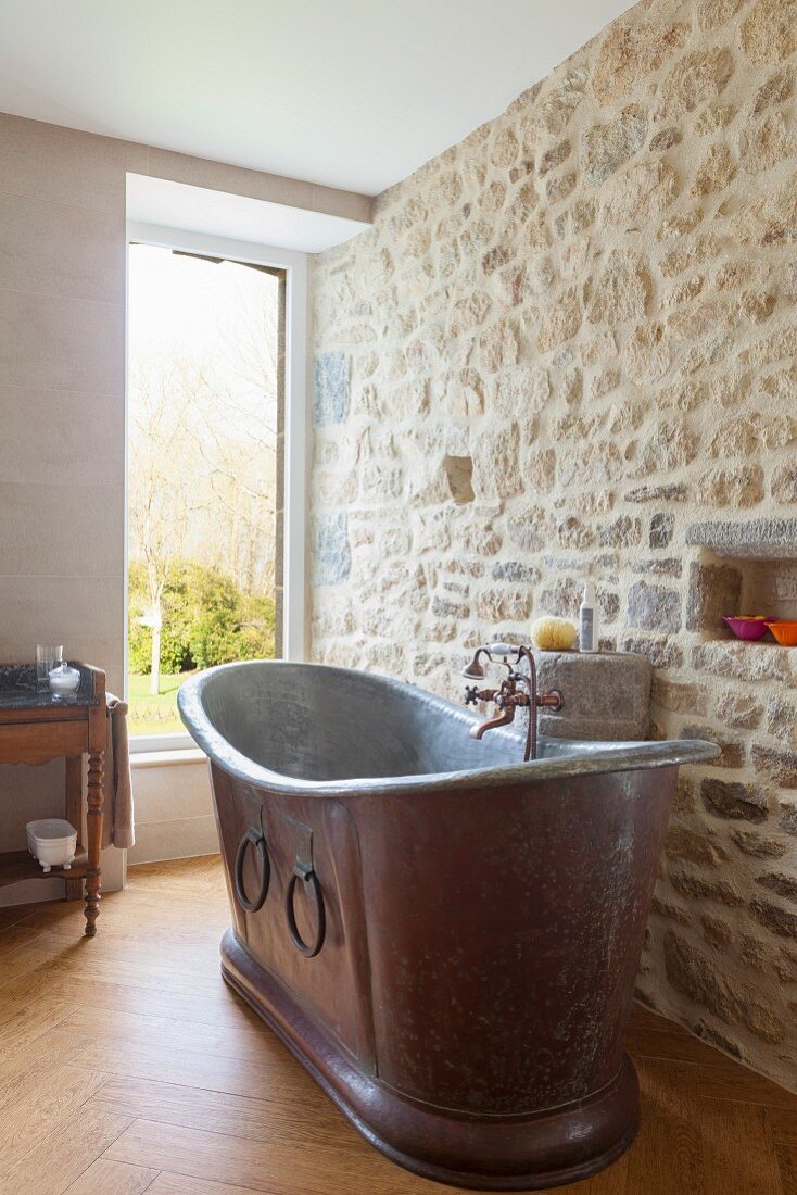 Vintage metal bathtub against stone wall in renovated bathroom with window