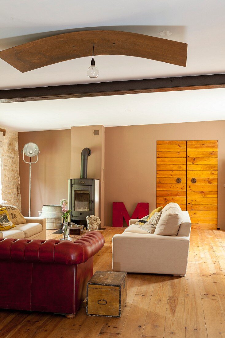 Rote Ledercouch und helle Couch in Wohnzimmer mit dielenboden und Schwedenofen eines renovierten Landhauses
