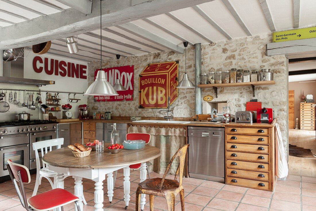 Offene Küche mit Essplatz, Stühle in verschiedenen Stilen um ovalem Holztisch in ländlicher Küche mit Vintage Blechschildern