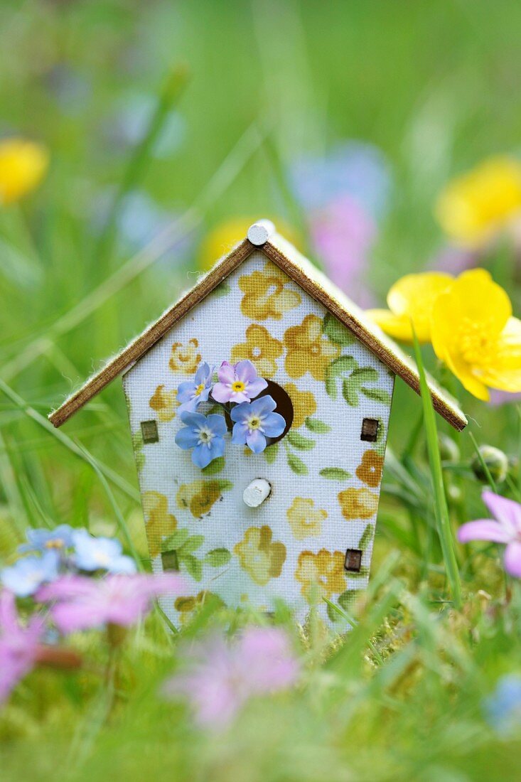 Bird nesting box painted with floral pattern amongst cranesbill, buttercups and forget-me-nots