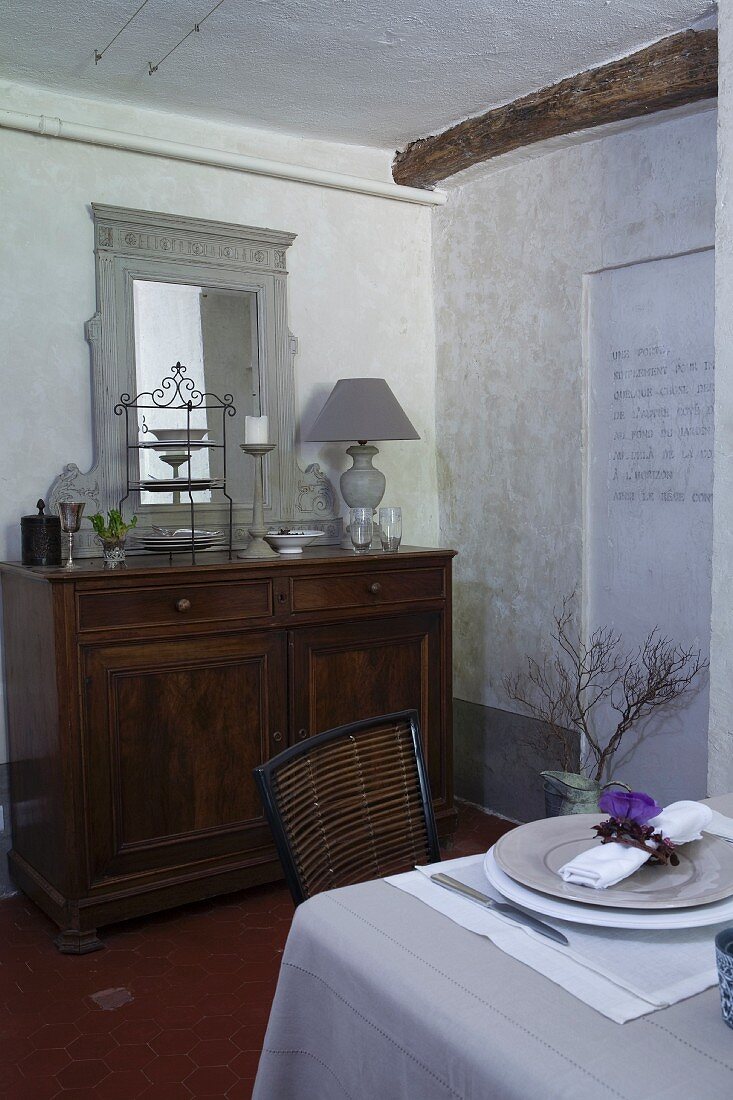 Old cabinet with mirror on top and set table in whitewashed dining room