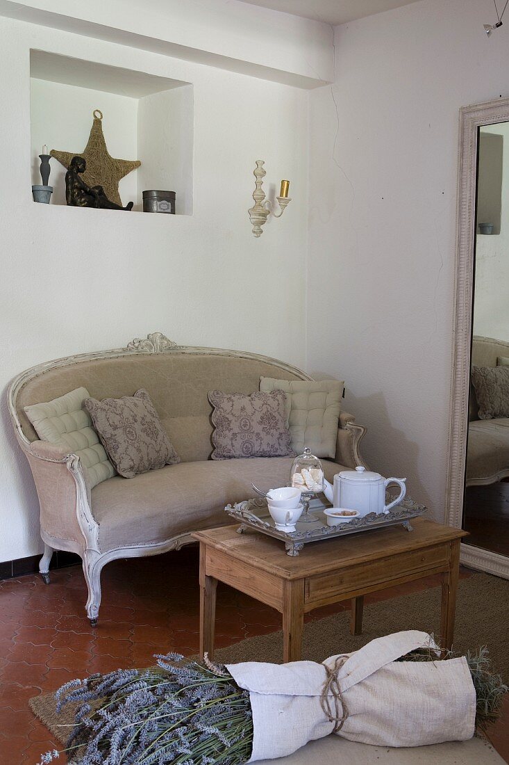 Old, stripped side table and antique couch next to full-length mirror; bunch of lavender in foreground