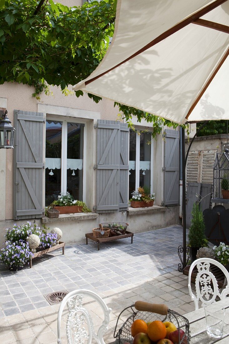 Terrassenplatz in gepflastertem Innenhof eines Landhauses mit grau lackierten Fensterläden