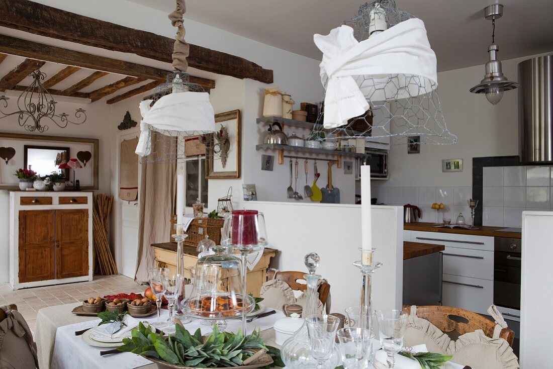Festlich gedeckter Tisch unter dekorierten Maschendraht-Pendelleuchten in offenem Landhaus-Wohnraum