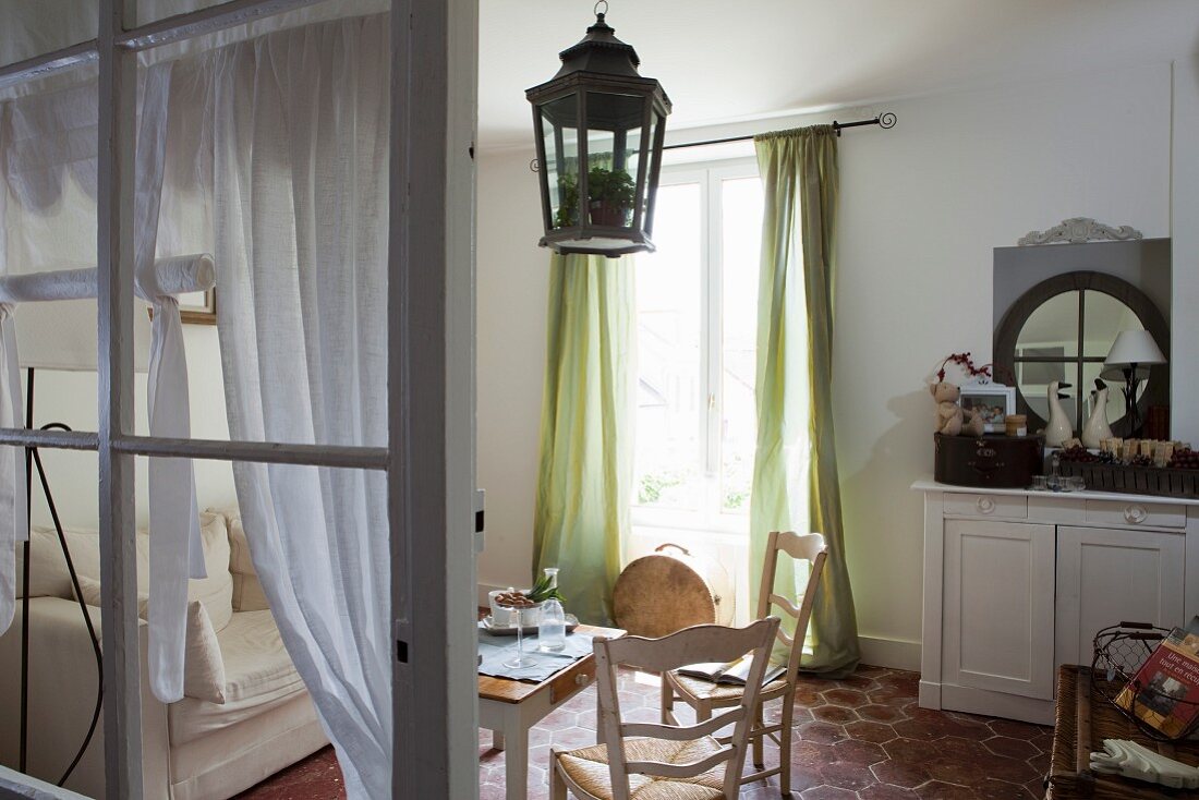 Tisch mit Holzstühlen vor Fenster mit bodenlangem grünem Vorhang und Landhausflair