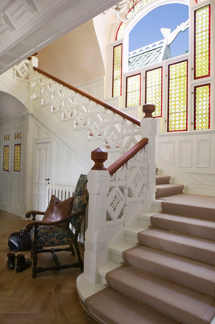 Grand staircase with ornate wooden balustrade and window with bulls'-eye panels in background