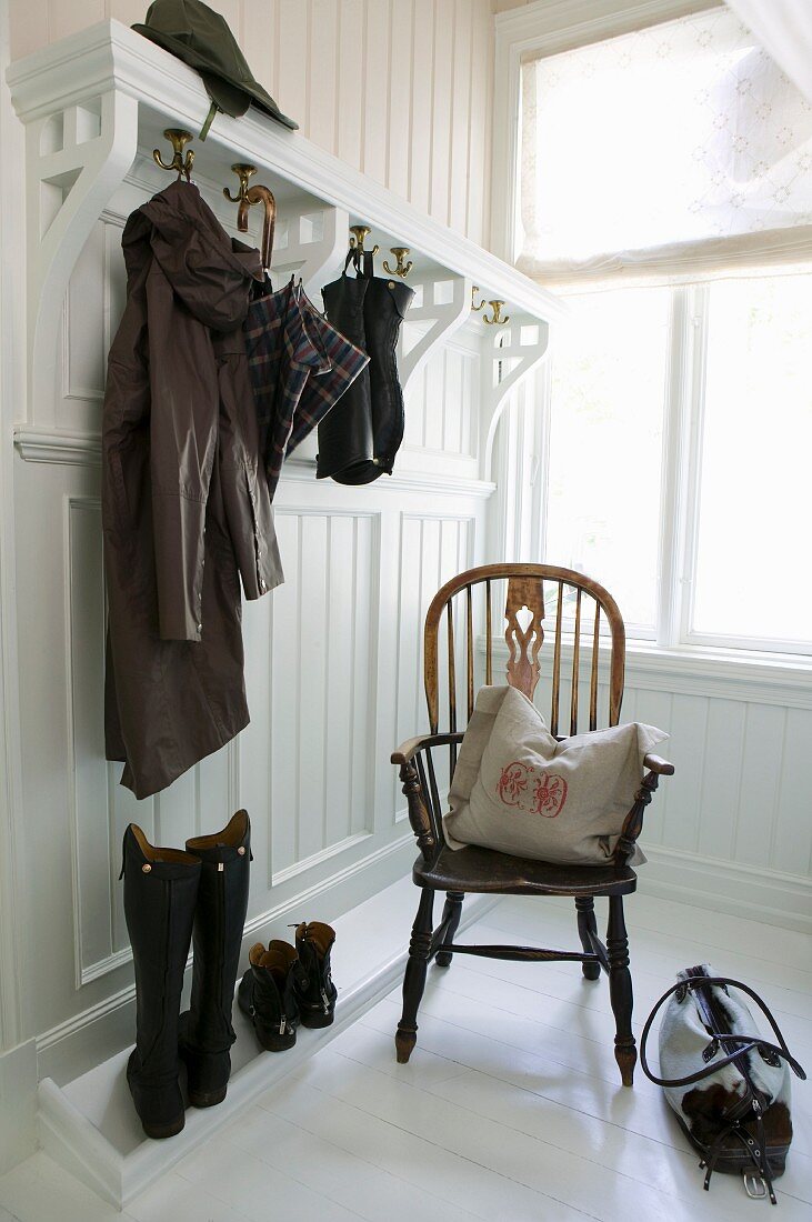 Windsor-Stuhl mit Kissen in weiss vertäfelter Garderobe mit hohen Stiefeln, Regenmantel und Schirm