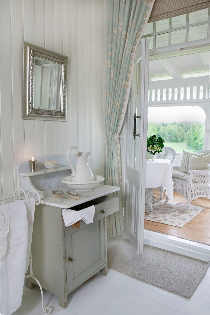 View from bedroom with traditional washstand through open door to seating area in conservatory