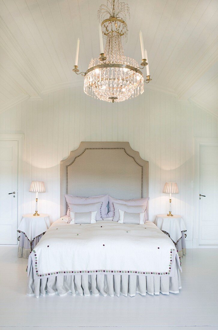 Opulenter Kristalleuchter über herrschaftlichem Doppelbett im weiss vertäfelten Schlafzimmer