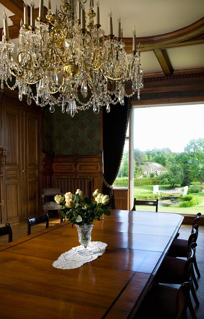 Kristallleuchter über langer Biedermeier Tafel in prächtigem Raum mit Panoramafenster zum Garten