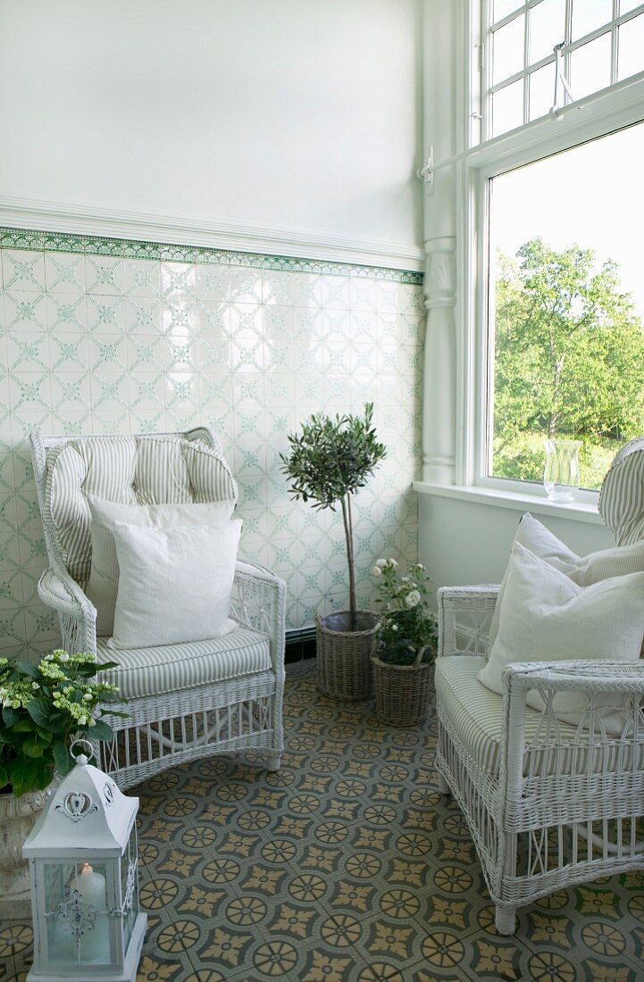 White wicker chairs with pale cushions in conservatory with tiled dado