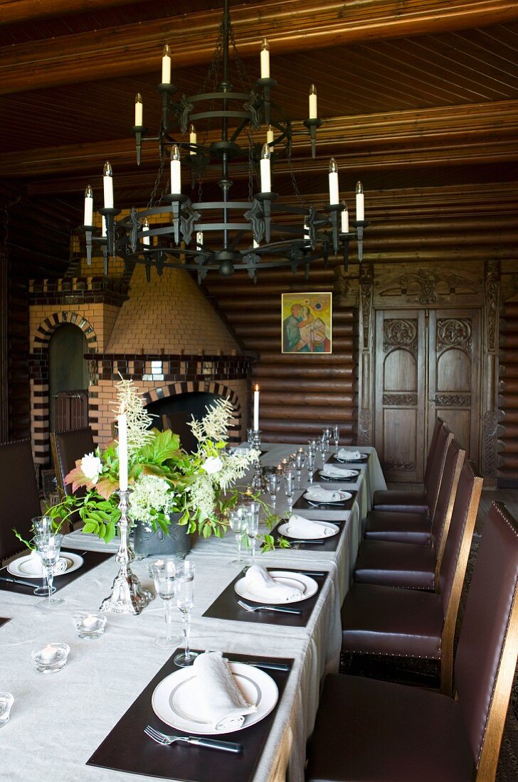 Wrought iron candle chandelier above set dining table and simple, leather-upholstered chairs in old dining room
