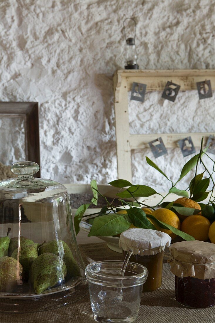 Birnen unter Glasglocke, frisch geerntete Zitronen und Marmeladengläser, alte Holzrahmen vor grob verputzter Wand