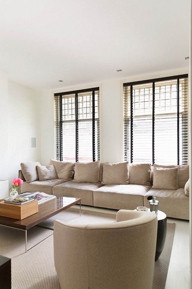 Sessel und Polstercouch in Naturfarben vor Fenster mit halbgeschlossener Jalousie, in modernem Wohnraum