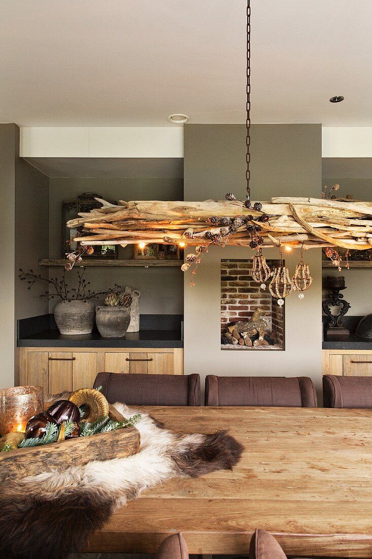Pendant lamp made from bundled sticks above solid-wood table with kitchen counter in background