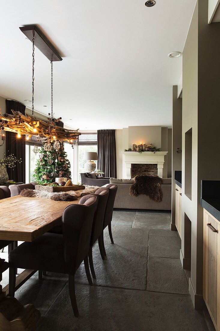 Lange Esstafel aus Holz und Polsterstühle in offenem Wohnraum, mit grossformatigem Steinfliesen