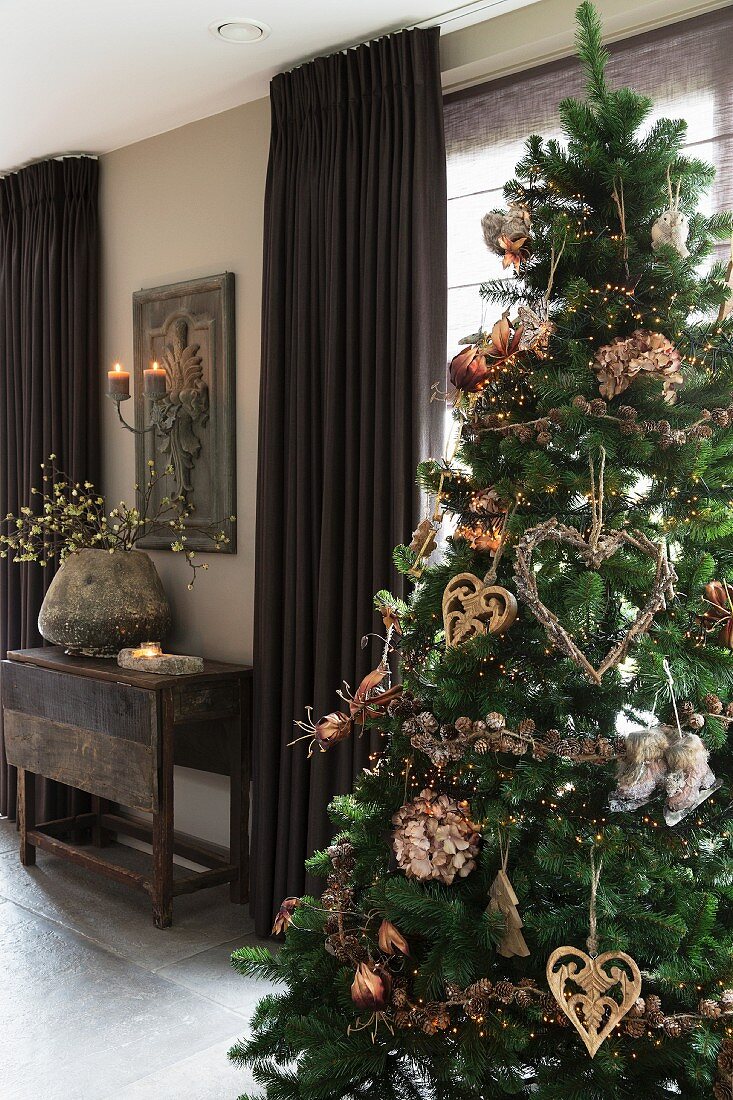 Geschmückter Weihnachtsbaum in Wohnraum, im Hintergrund braune, bodenlange Vorhänge an Fenster