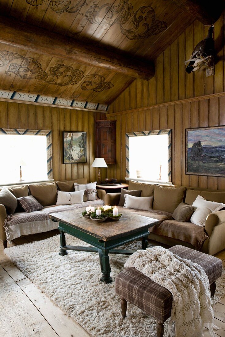 Gemütliche Sitzecke, Polsterhocker und Sofas um Couchtisch in rustikalem Wohnzimmer eines Holzhauses