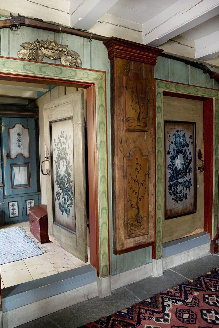 Vorraum mit bemalten Wänden in altem Holzhaus, Blick durch offene Tür auf Schrank
