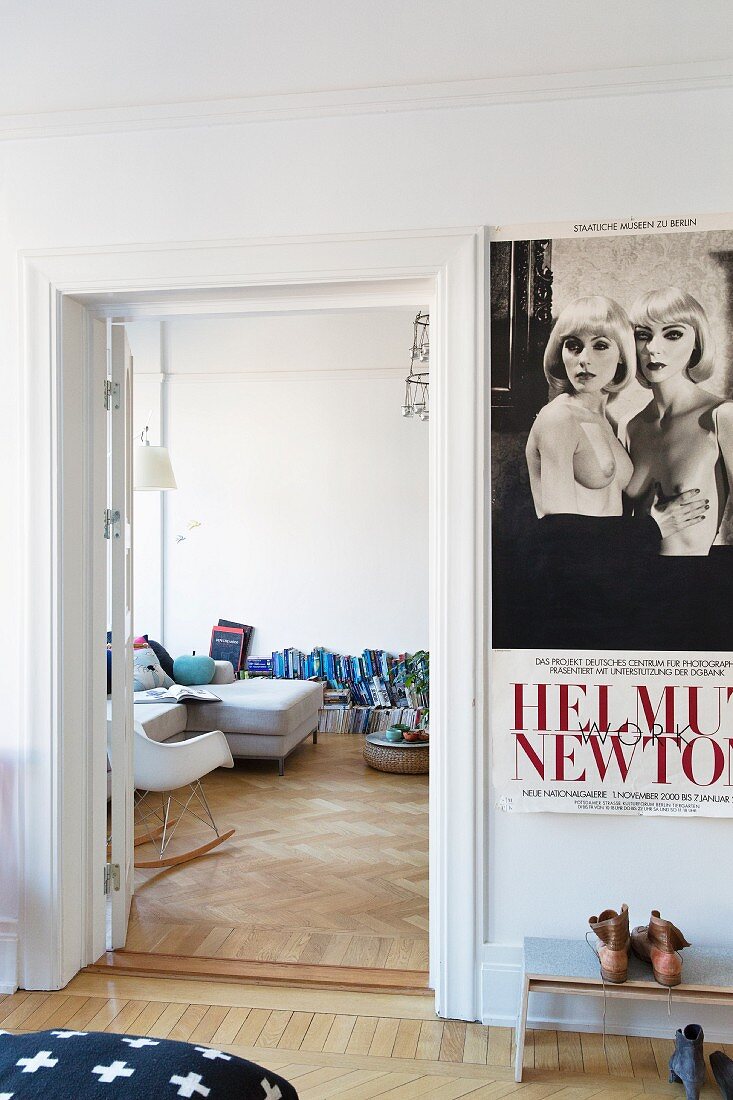 Vintage Plakat über Schuhbank im Schlafzimmer, daneben Blick in Wohnraum mit Klassiker Schaukelstuhl und Bücherstapeln