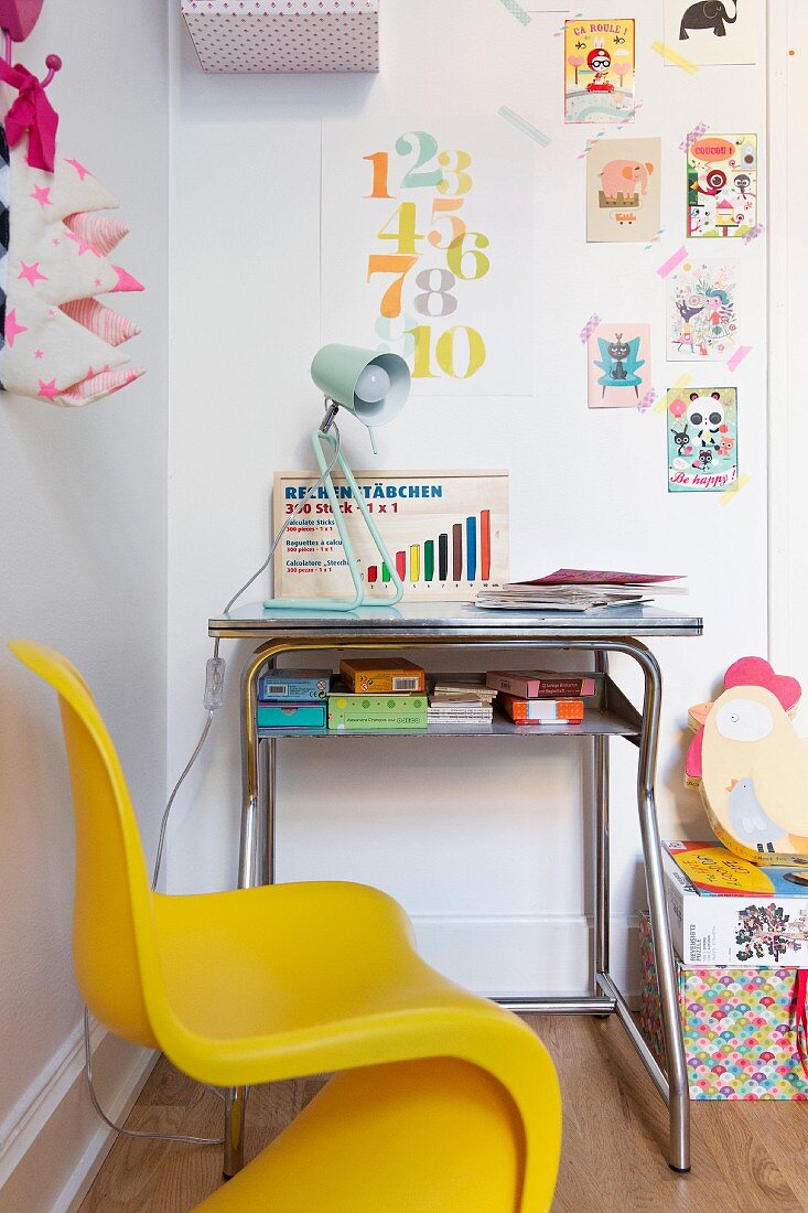 Yellow, child's chair at small desk below postcards and stamped numbers stuck to wall using washi tape