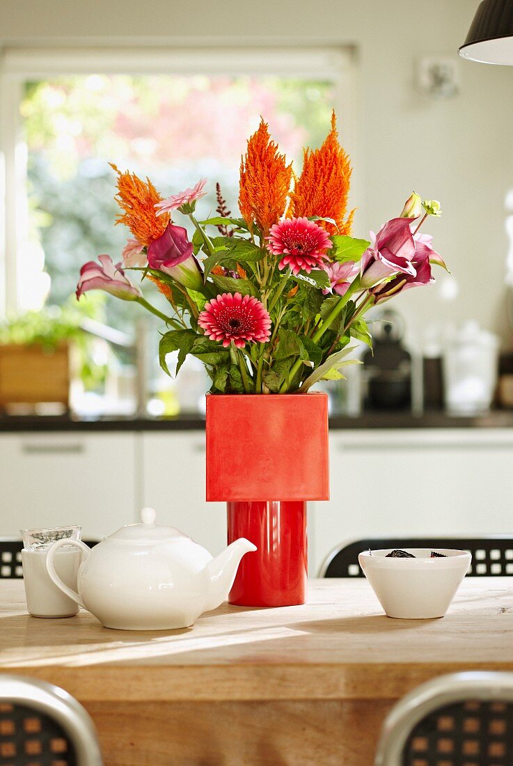 Vase of gerbera daisies and calla lilies in various shades of red in red vase on dining table