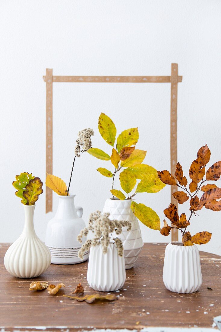 Branches of autumnal leaves in white, ceramic vases on table