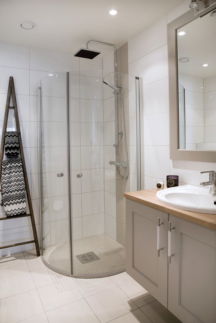 Waschtisch mit Unterschrank neben Duschbereich mit gebogenen Glastüren in modernem Bad