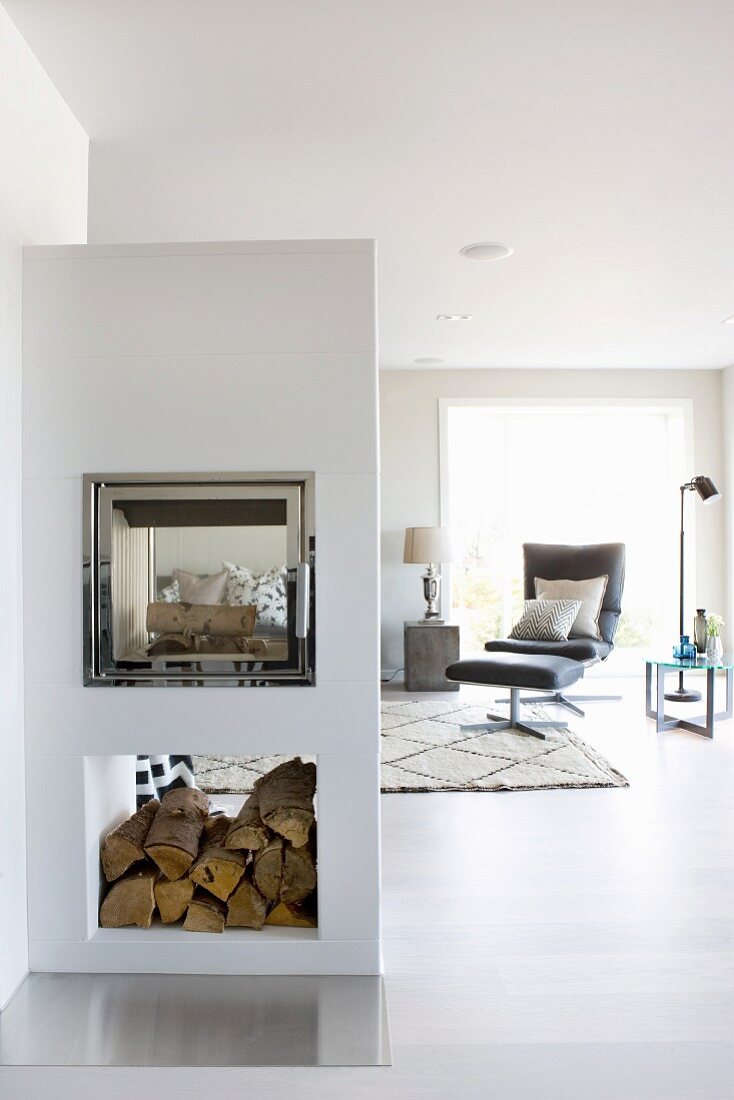 Masonry fireplace in open-plan minimalist interior with Lounge chair and footstool in background