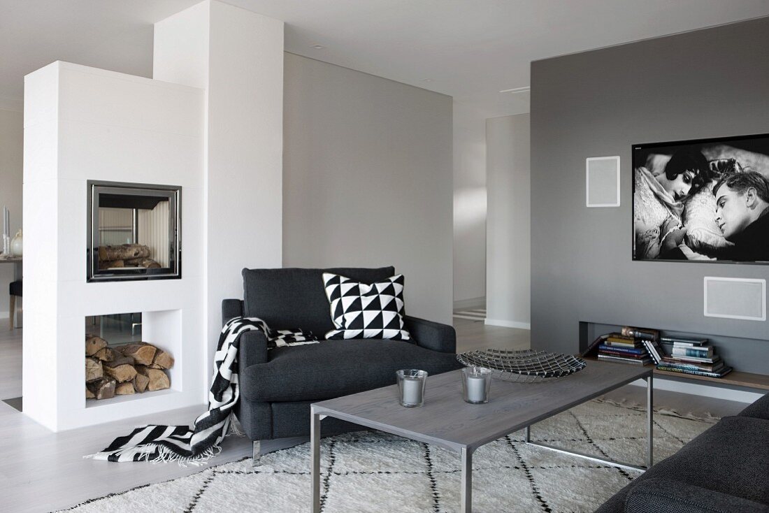Grau getönter Loungebereich mit filigranem Couchtisch und schwarzer Sessel, seitlich gemauerter Kamin