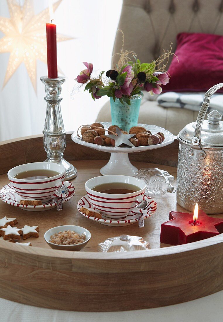 Weihnachtliche Teepause - Teetassen und Schale mit Nüssen neben Kerzenständer mit brennender Kerze auf Tablett