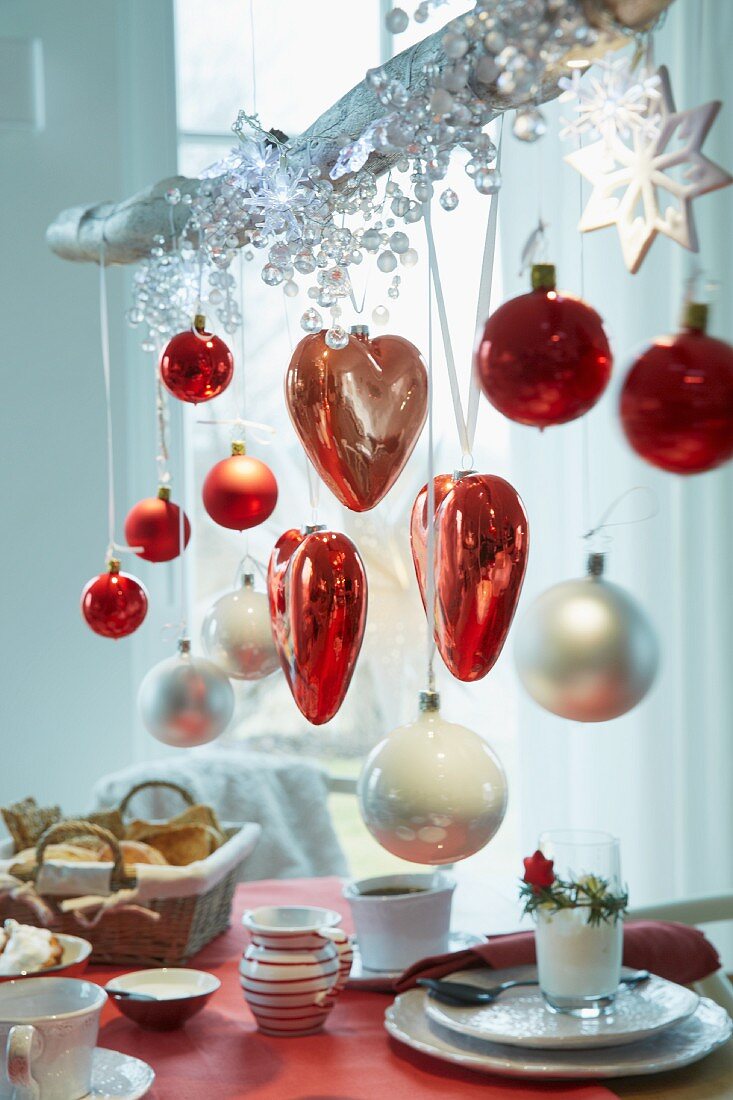 An Ast aufgehängte Herzen und Weihnachtsbaumkugeln in Rottönen über Frühstückstisch