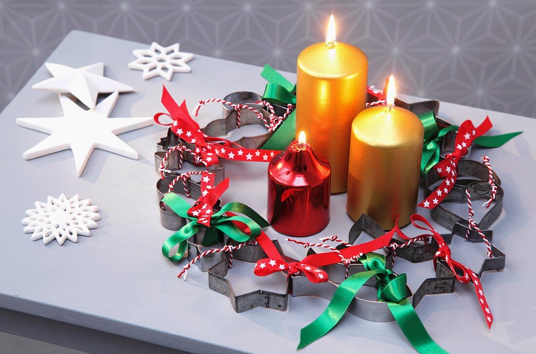 Weihnachtlicher Kranz aus Plätzchenausstechern und Schleifenbändern und drei Kerzen