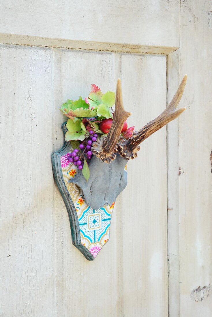 Stylised hunting trophy on patterned plaque decorated with plastic leaves and fruit