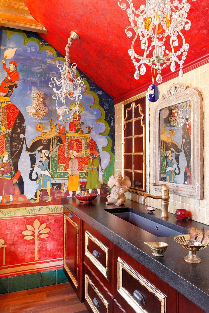 Indian-style mural on wall of traditional kitchen with ornate chandeliers with crystal pendants above kitchen counter