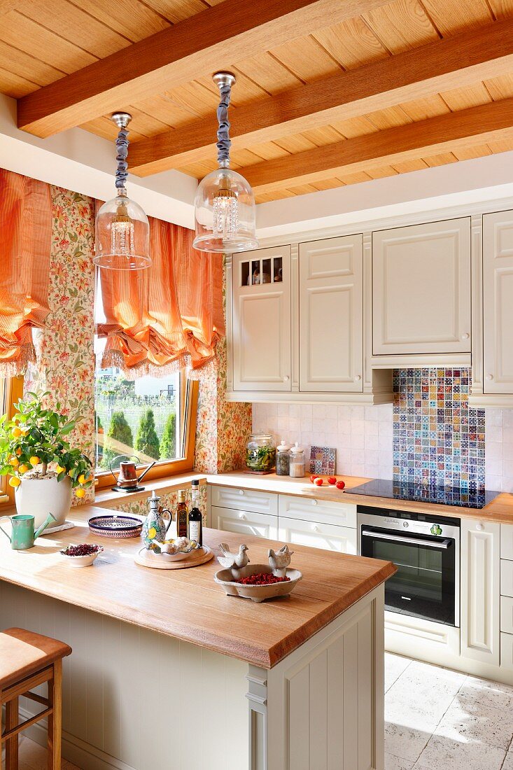 Küche in hellem Landhausstil mit Frühstückstheke, unter Hängeleuchten an Holzdecke